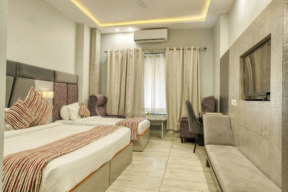 A hotel room with two beds, a desk, a chair, and a TV.