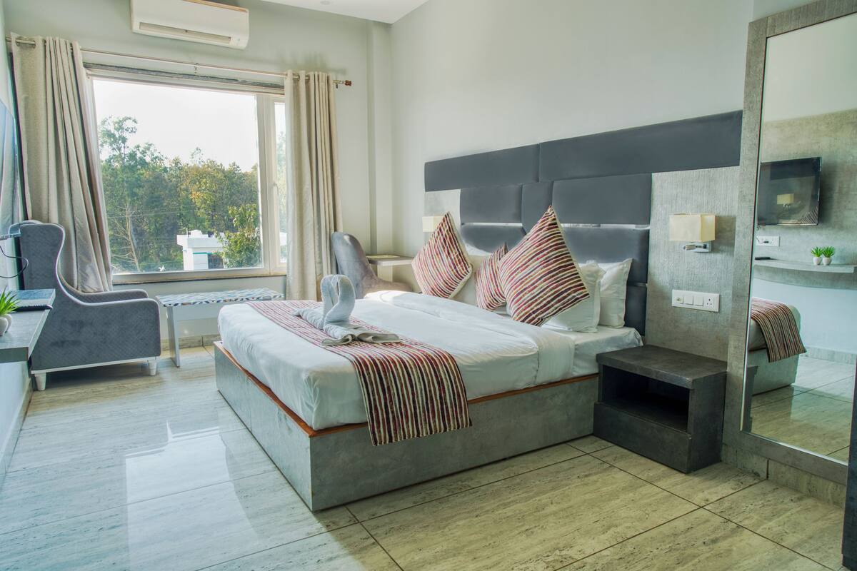 A modern hotel room with a large bed, a desk, a chair, and a view of the outdoors.