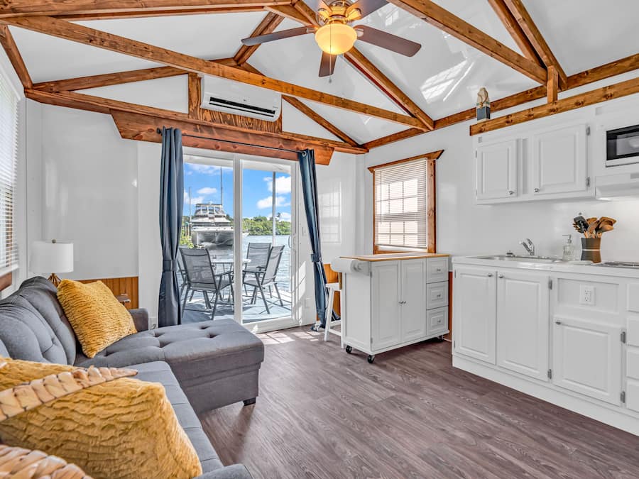 A spacious living area with a gray sectional sofa, wooden beams, and a ceiling fan.