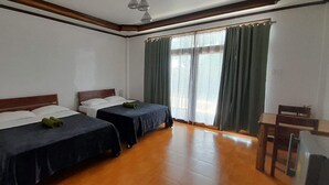Een kamer met twee bedden, een houten vloer, een raam met gordijnen en een klein tafeltje.