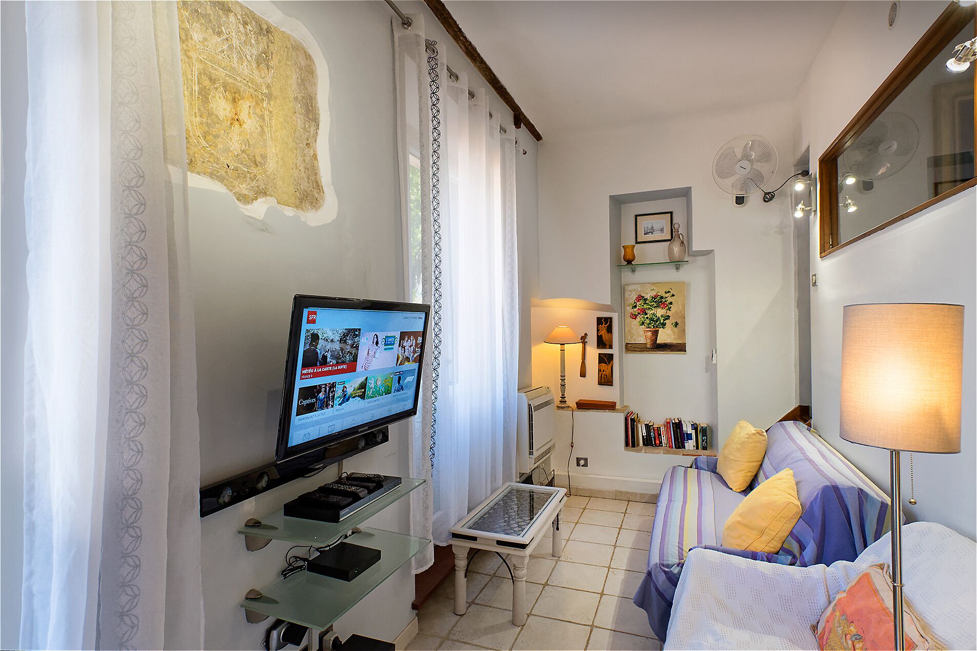 Un salon avec une télévision, un canapé, une table basse et une lampe.