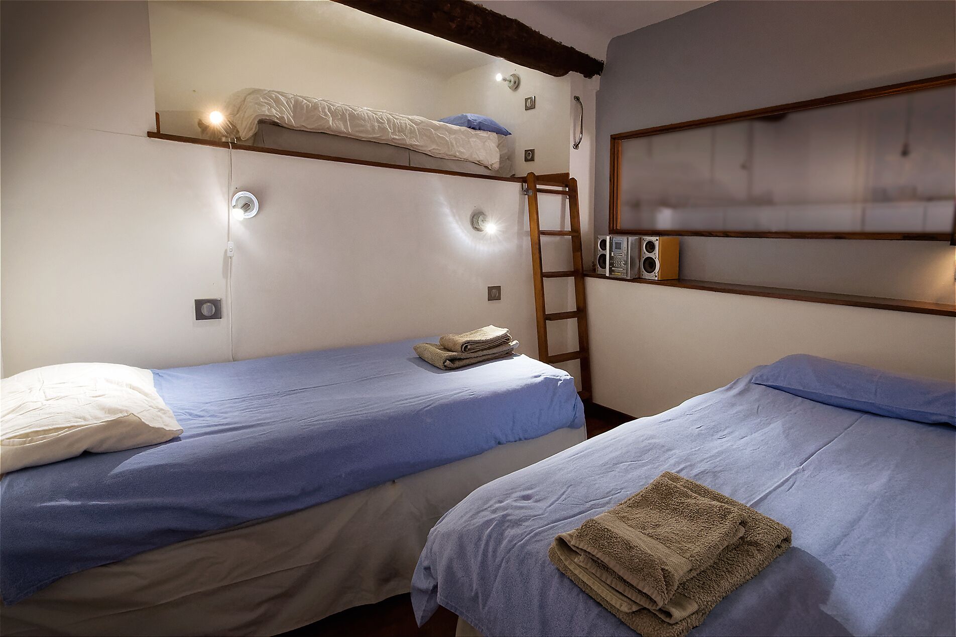 Une pièce avec deux lits superposés, une échelle et un haut-parleur fixé au mur.