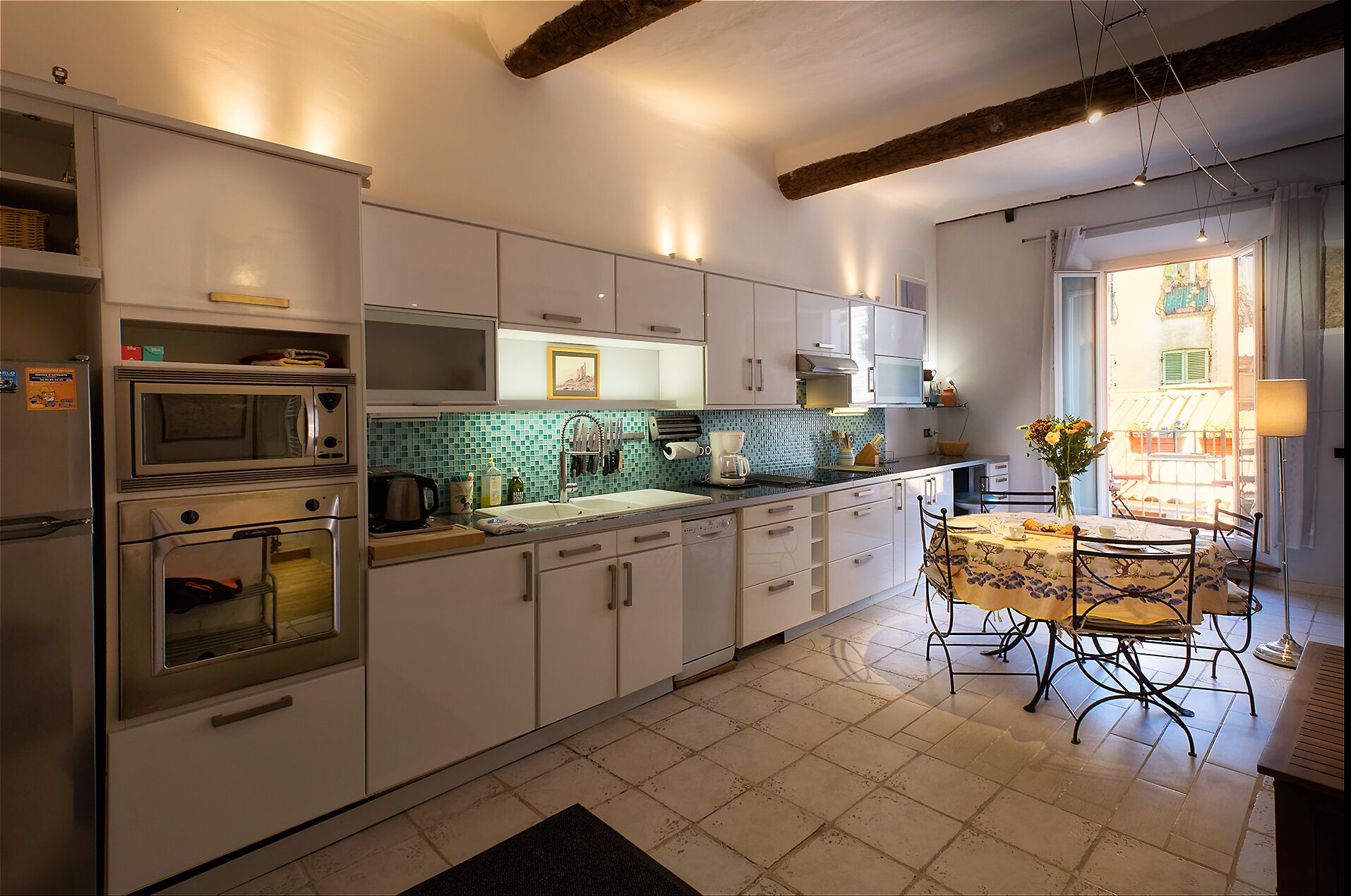 Une cuisine avec des meubles blancs, un pare-feu en carrelage et un coin repas comprenant une table et des chaises.
