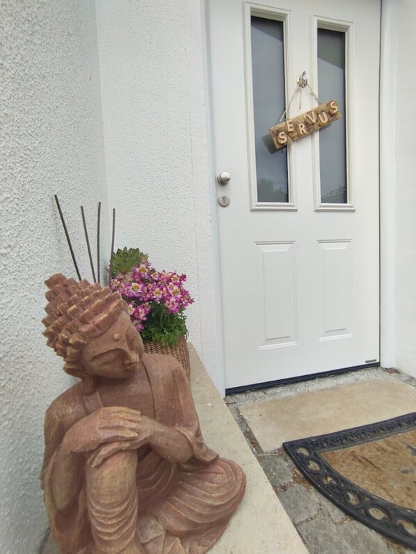 A statue of a seated figure, a door with a 'SERVUS' sign, and a planter with flowers. - An elegant, modern, and spacious home (Tittmoning)