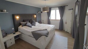 Ein Schlafzimmer mit Bett, Nachttischen, Vorhängen an einem Fenster und einer Tür.