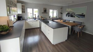 Eine moderne Küche mit weißen Schränken, einer zentralen Kochinsel und einem Essbereich mit Holztisch.