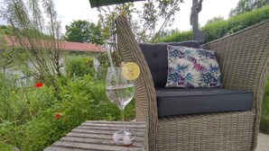 Ein Korbssessel mit floralem Kissen und einem kleinen Holztisch mit einem Weinglas und einer Zitrone.