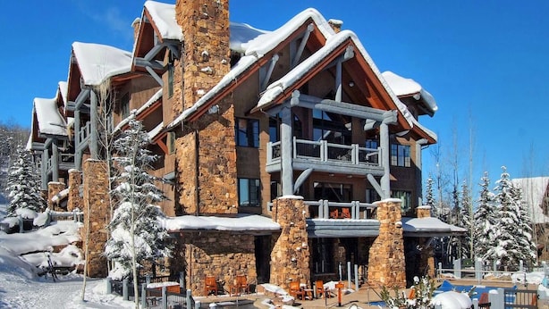 A multi-story lodge with stone and wood exterior, snow-covered roof, and outdoor seating area. - Bearpaw D1 4 Bedroom Condo by RedAwning (Avon)