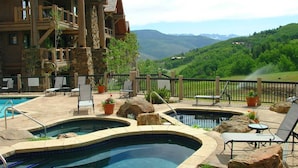 A pool area with two hot tubs, lounge chairs, and a stone building with a view of a mountainous landscape. - Bearpaw D1 4 Bedroom Condo by RedAwning (Avon)