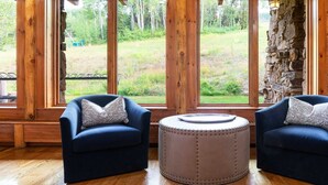 A room with two blue armchairs, a round ottoman, and large windows offering a view of a grassy outdoor area. - Bearpaw D1 4 Bedroom Condo by RedAwning (Avon)