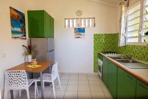 Une cuisine de taille réduite avec des meubles de couleur verte, un pare-feu en carrelage, une table à manger avec des chaises et une horloge au mur.
