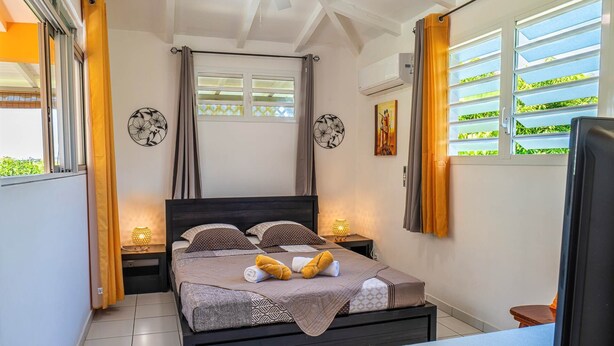 Quarto com cama, duas mesinhas de cabeceira, ventilador de teto, janela com cortinas e aparelho de ar condicionado.