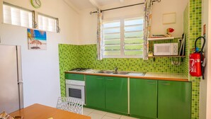 Cozinha com armários verdes, micro-ondas, pia e janela com persianas.