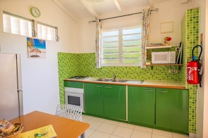 Une cuisine avec des meubles de rangement verts, un four à micro-ondes, un évier et une fenêtre avec des volets.