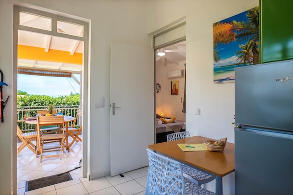 Une cuisine compacte équipée d’un réfrigérateur, d’une table à manger avec des chaises et offrant une vue sur le balcon extérieur.