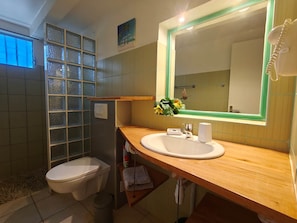 Un baño con tocador de madera, un lavabo blanco, un espejo y cabina de ducha con mampara de vidrio.