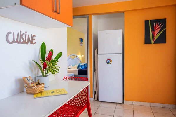 Una kitchenette con encimera blanca, una silla roja, una planta en maceta y un paquete de café.