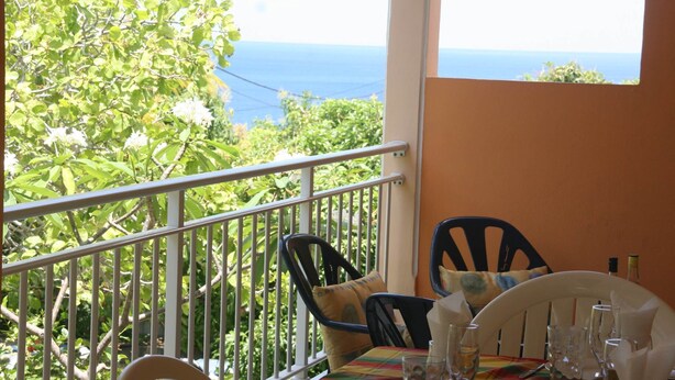 Un balcone con tavolo apparecchiato per mangiare, affacciato su un giardino rigoglioso e il mare.
