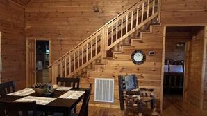 Interno di una baita in legno con zona pranzo, una scala e un angolo soggiorno.