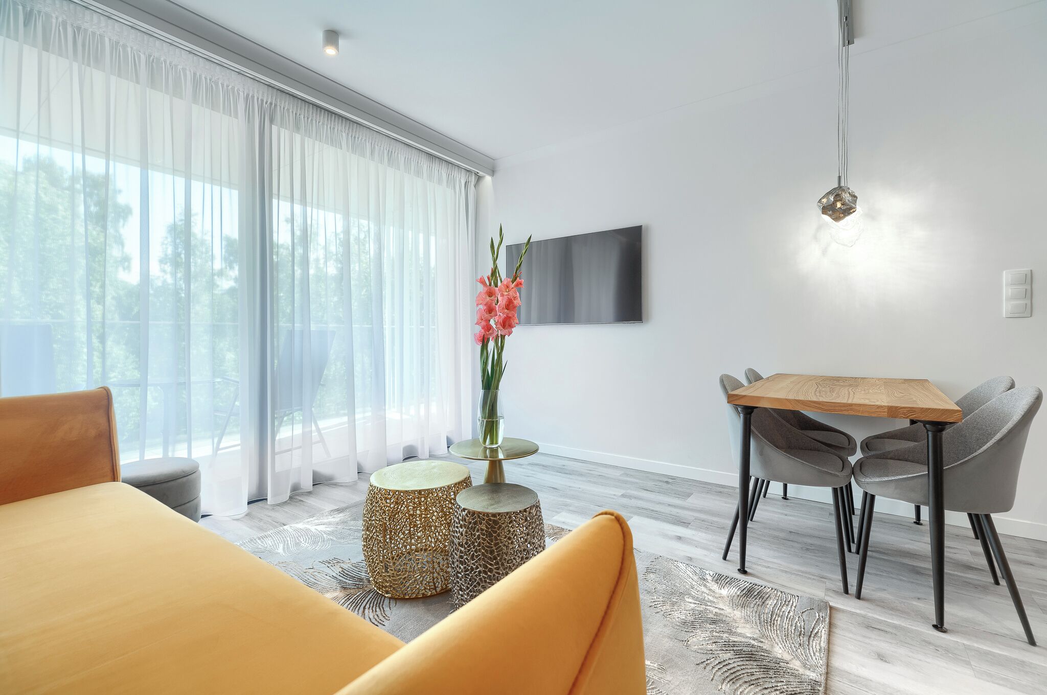 En moderne stue med sofa, spisebord med stole, fjernsyn ophængt på væggen og en vase med blomster.