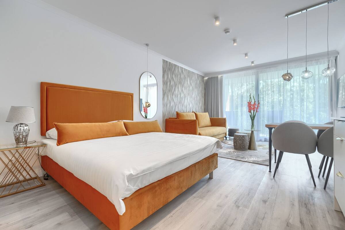 A modern hotel room with a large bed, a desk, and a dining area.