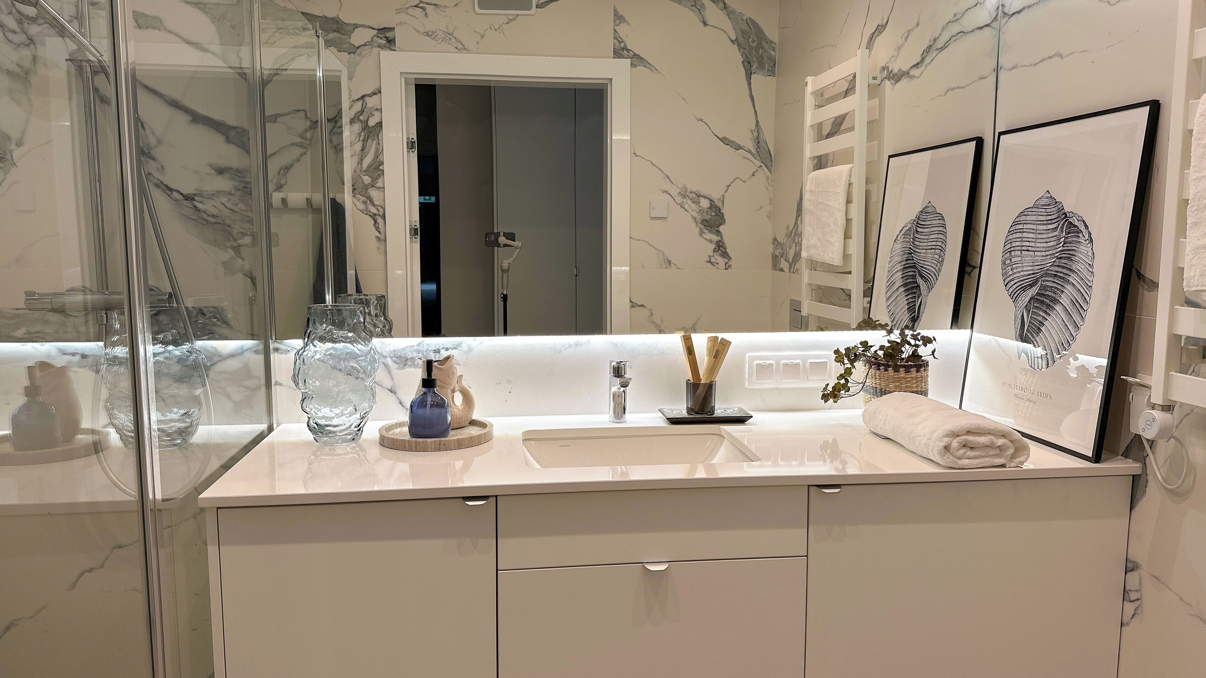 A modern bathroom with a marble backsplash, a glass shower enclosure, and a vanity with a sink and decorative items.