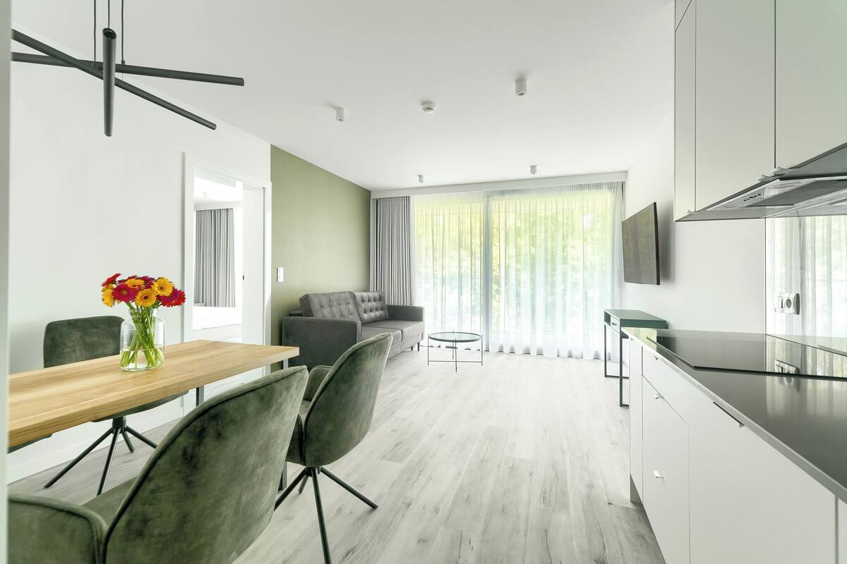 A modern kitchen with a dining area, grey upholstered chairs, a wooden table, and a vase of flowers.