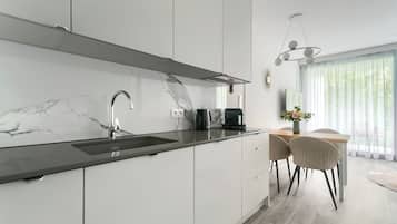 Una cocina moderna con armarios blancos, salpicadero de mármol y encimera negra. Hay una cafetera sobre la encimera y un comedor con mesa y sillas.