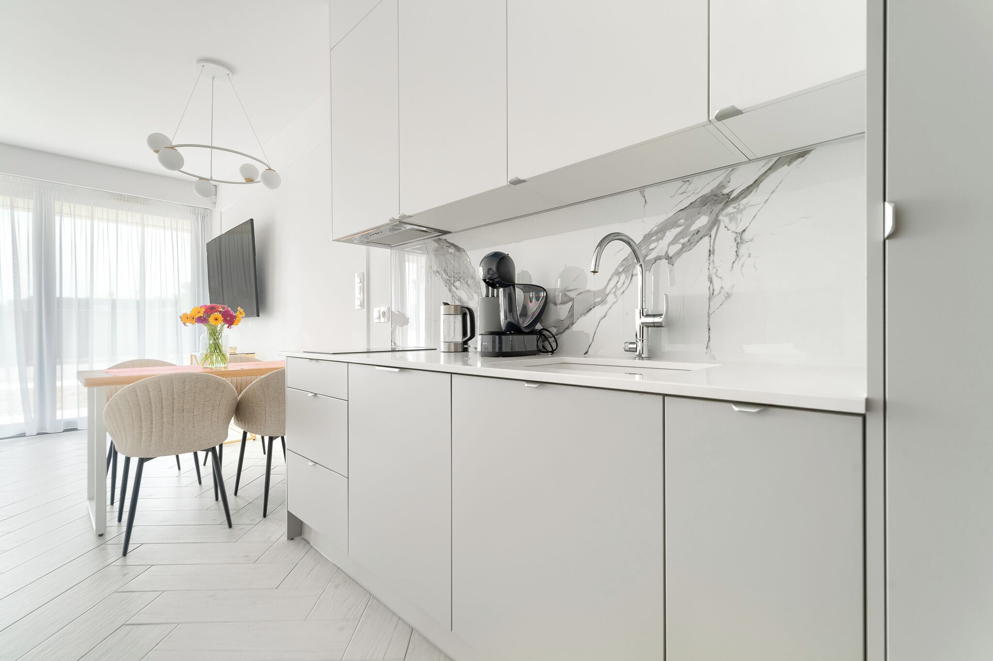 Eine moderne Küche mit weißen Schränken, einer Marmor-Spritzschutzwand und einem Essbereich mit Holztisch und -stühlen.