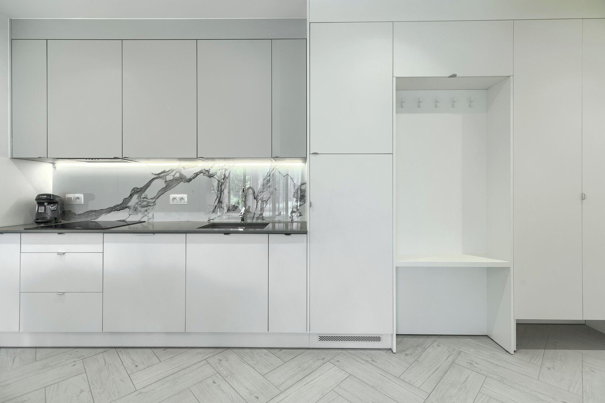 Eine moderne Küche mit weißen Schränken, einer Marmor-Spritzschutzwand und einer eingebauten Sitzbank.