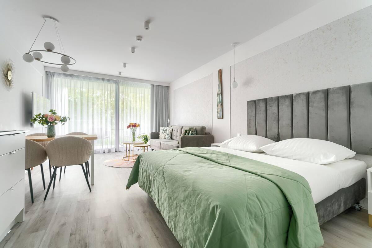 A modern bedroom with a large bed, a dining area with chairs, a sofa, and a small table with flowers.
