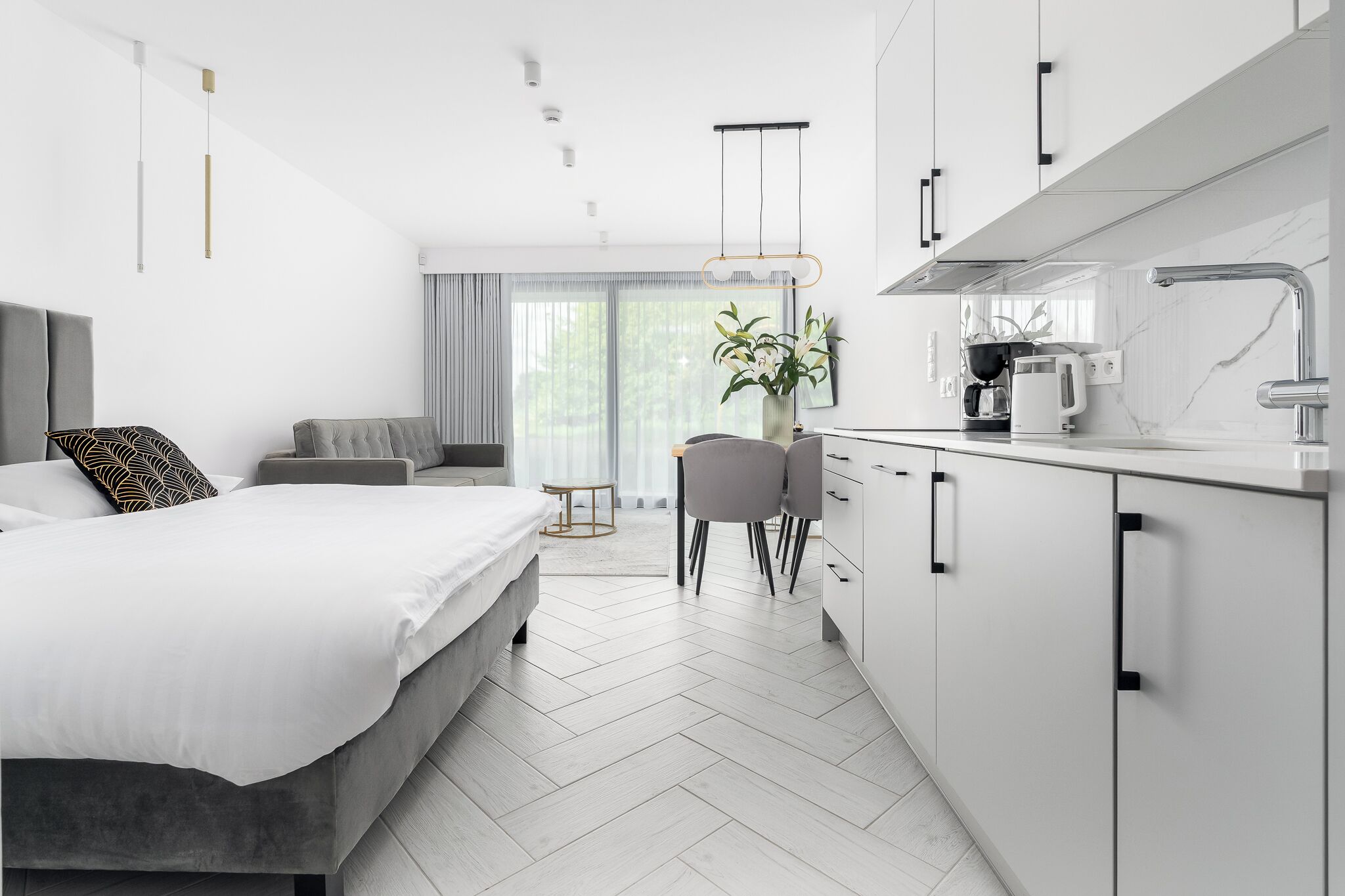 A modern hotel room with a bed, a sofa, a dining area, and a kitchen.