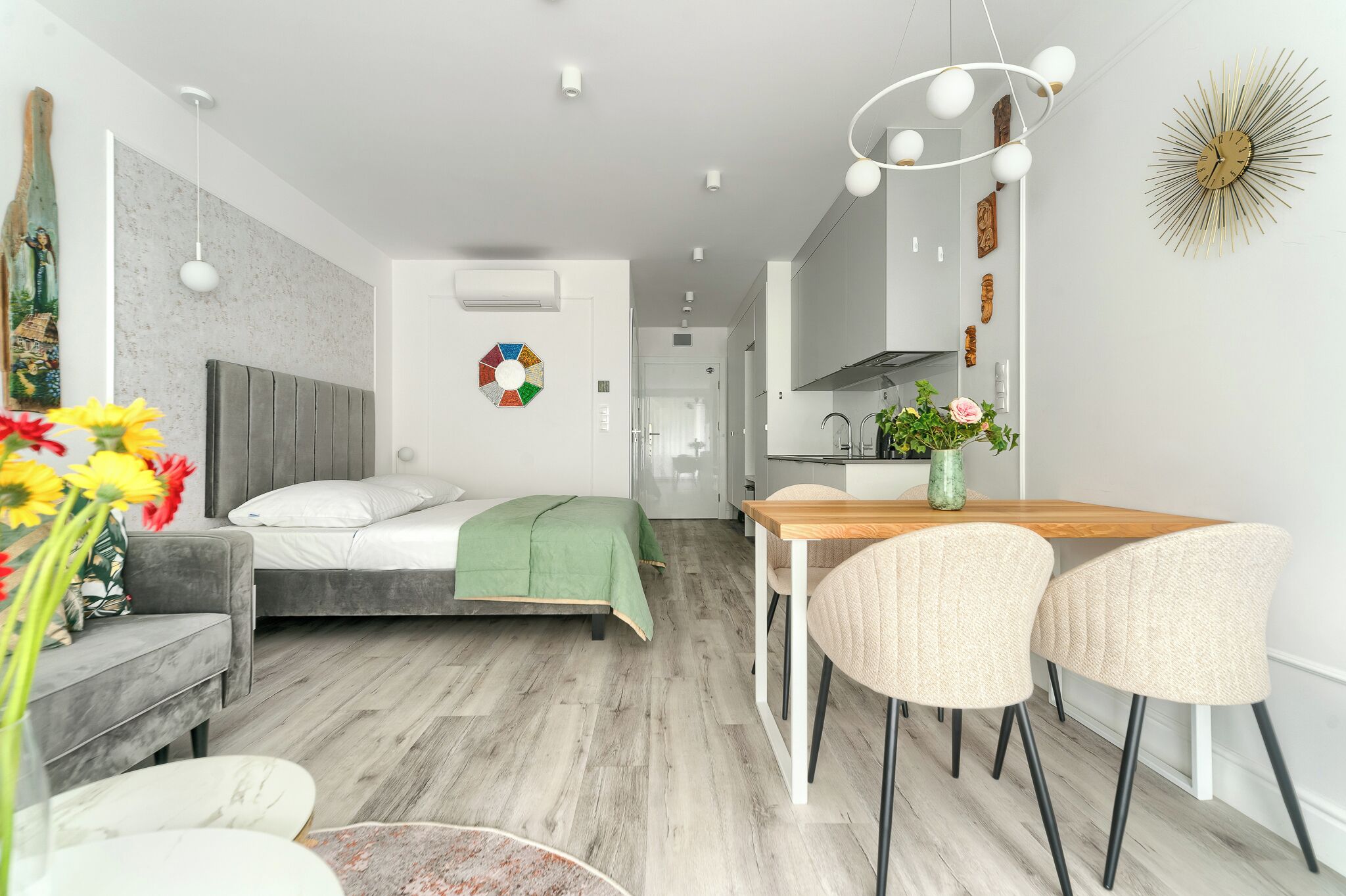 Une chambre moderne avec un lit, une table de chevet et un plaid vert. On y trouve également un coin repas avec une table en bois et deux chaises.