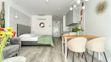 Une chambre moderne avec un lit, une table de chevet et un plaid vert. On y trouve également un coin repas avec une table en bois et deux chaises.