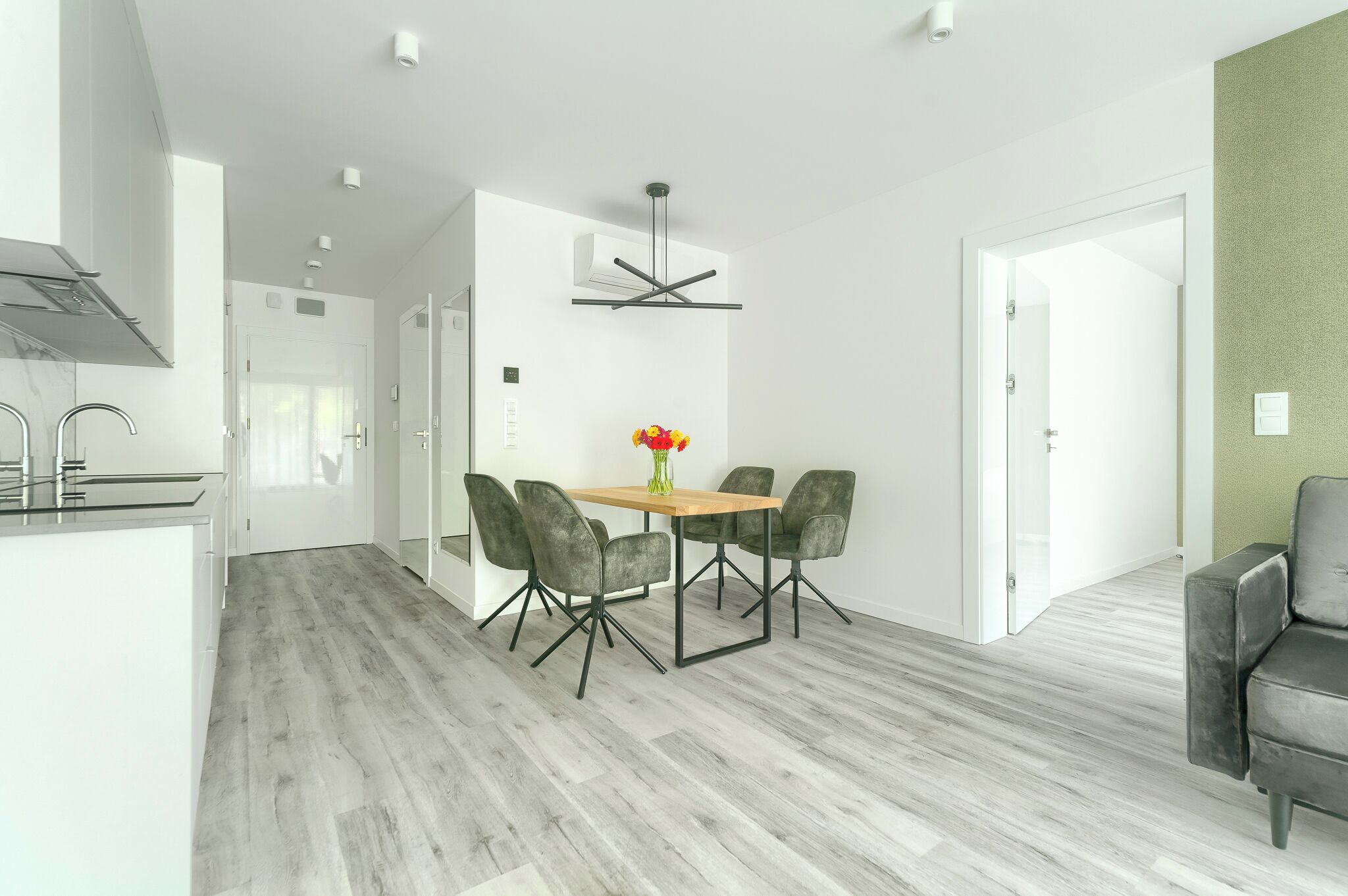 A modern kitchen with white cabinets, a built-in stove, and a dining area with a wooden table and four chairs.