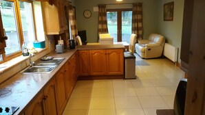 A kitchen with wooden cabinets, a sink, and a stove. There is a dining area with a table and chairs. - Slieve Anierin House (Gortnawaun)