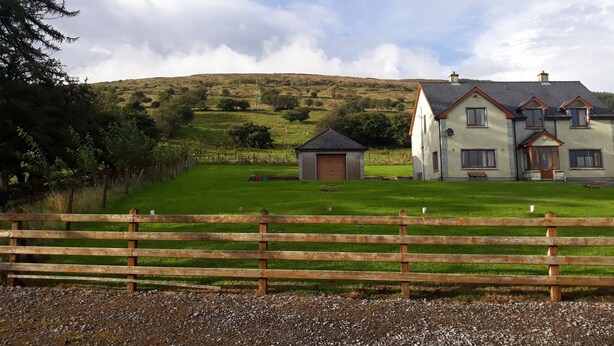 A two-story house with a large front lawn, a wooden fence, and a hill in the background. - Slieve Anierin House (Gortnawaun)