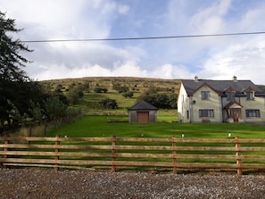 A two-story house with a large front lawn, a wooden fence, and a hill in the background. - Slieve Anierin House (Gortnawaun)