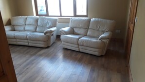 A room with two beige leather sofas, wooden flooring, and large windows. - Slieve Anierin House (Gortnawaun)