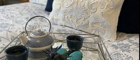 A bed with a decorative pillow, a tray with a teapot, cups, and macarons.