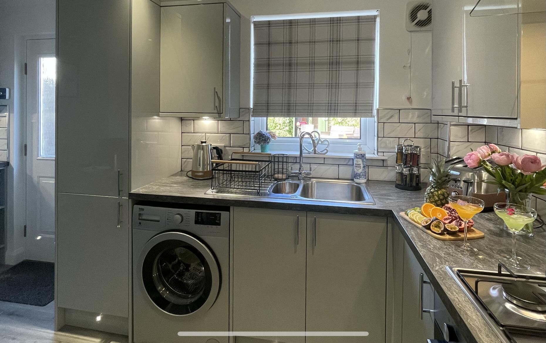 Una cocina moderna con lavadora incorporada, un ventanal con vistas y una encimera con diversos utensilios de cocina y un bol de frutas.