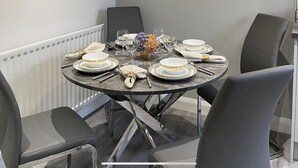Un tavolo da pranzo rotondo con piatti bianchi e dettagli dorati, circondato da sedie nere.