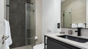 A modern bathroom with a glass shower enclosure, a white toilet, and a sink with a black faucet. - The Signature G07 (Cape Town)