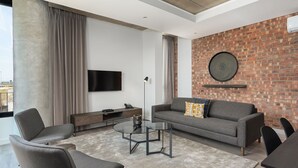 A modern living room with a grey sofa, a glass coffee table, and a brick accent wall. - The Signature G07 (Cape Town)