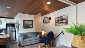 A modern kitchen with a stainless steel refrigerator, a dining area with a wooden table and chairs, a gray sofa with blue cushions, and a patterned rug. - Lakeside Living with HotTub, Kayaks, Paddleboard; close to Olympic National Park (Port Angeles)