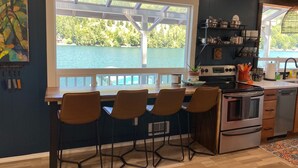 A kitchen with a large window overlooking a lake, a bar area with stools, and modern appliances. - Lakeside Living with HotTub, Kayaks, Paddleboard; close to Olympic National Park (Port Angeles)