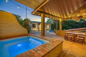 Piscina com borda de tijolos, pérgola de madeira e área de estar externa.