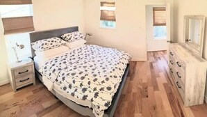Une chambre à coucher comprenant un lit, une table de chevet, une commode et une fenêtre avec des stores.