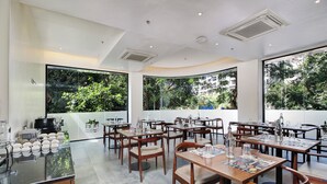 Un comedor moderno con mesas y sillas, amplias ventanas con vistas a zonas verdes y un interior limpio y luminoso.