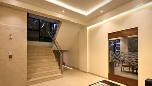 Un interior moderno con una escalera de mármol, una mesa de recepción y un panel de vidrio que refleja el paisaje exterior.